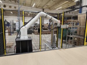 Stanowisko zrobotyzowane do zbijania skrzyń – robot przemysłowy za siatką bezpieczeństwa